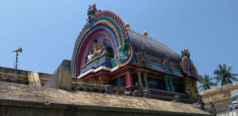 Barrel-shaped roof of a shrine with a colourful arched front holding seated figures, under a blue sky