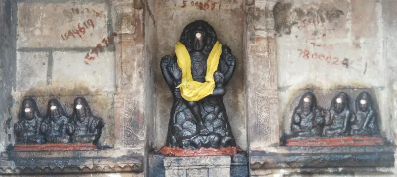 Dark stone figure in a yellow cloth, with three small figures carved on each side