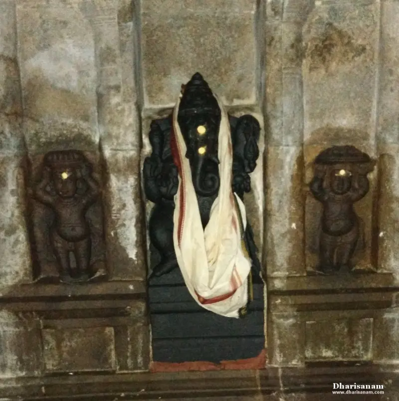 A black stone Vinayakar draped in a white cloth, standing in a niche between two small carved figures