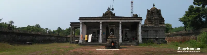 A pillared stone hall with clothes hung out to dry, and a tower of the sanctum at right beyond a small lamp pavilion.