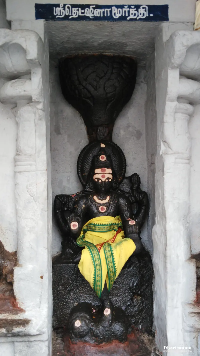 Seated four-armed idol in yellow cloth under a carved tree canopy