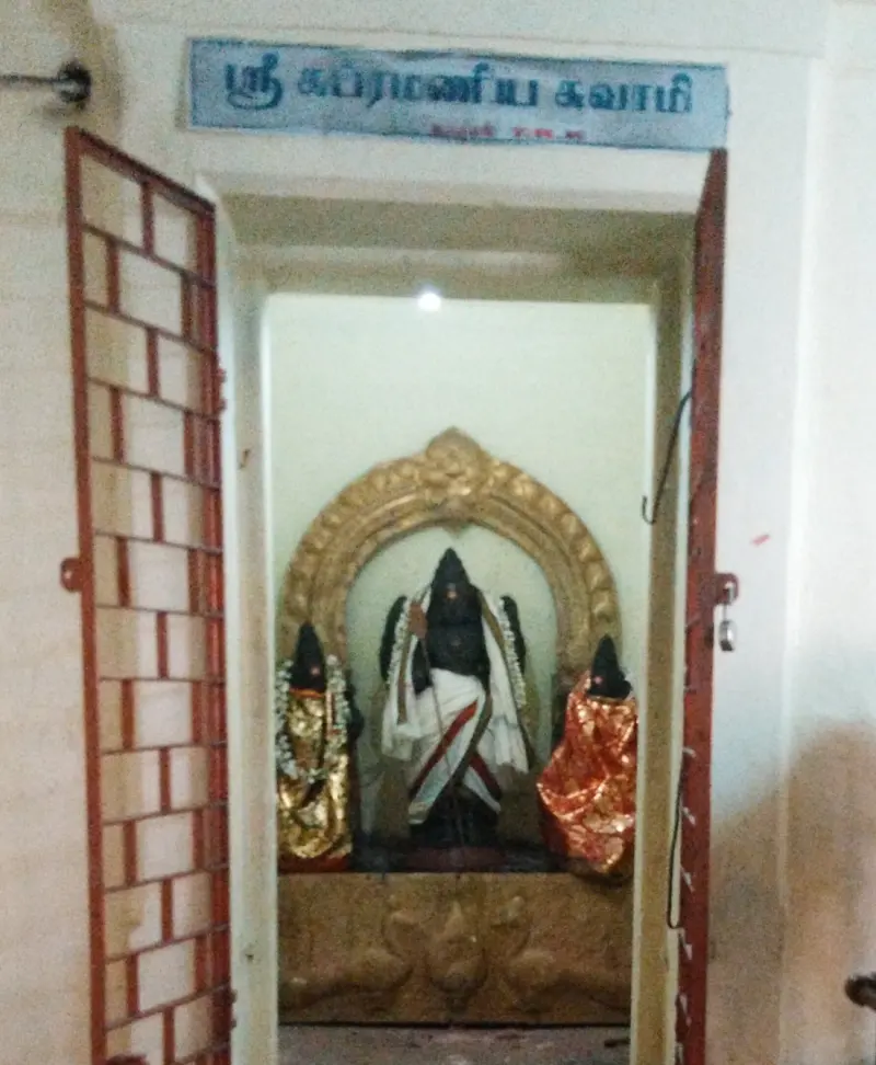 Three dressed dark idols stand under a gilded arch; a blue name board in Tamil hangs over the open doors.