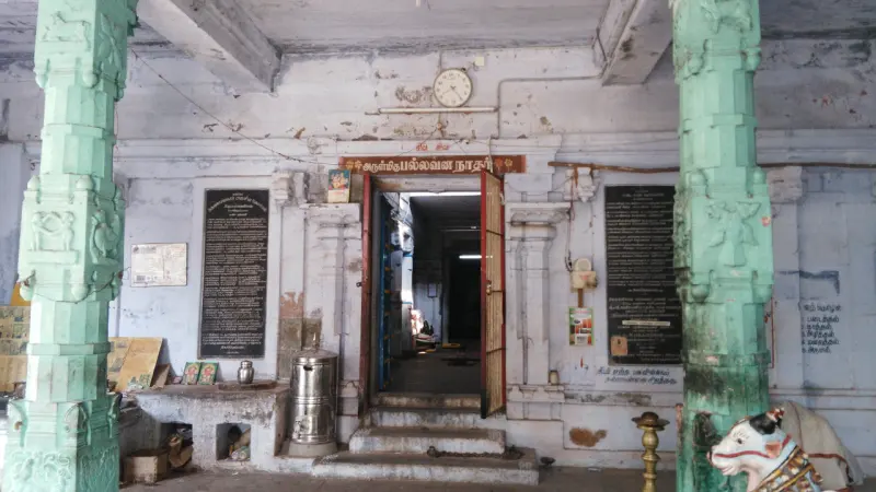 A pillared hall with green columns, a doorway with notice boards on each side and a Nandi at the right edge