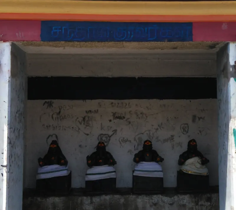 Four small black seated figures in white cloth, in an open shrine