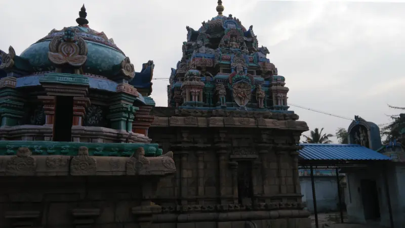 A domed shrine roof and a taller painted tower rising above stone walls, with a blue shelter beyond.