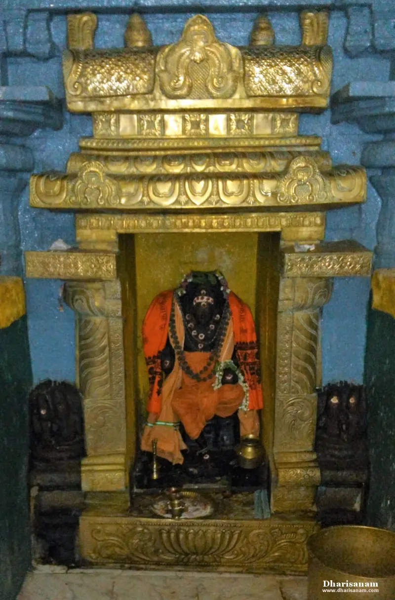 A seated dark idol wearing saffron cloth and beads sits in a gold-coloured niche with two small figures beside it