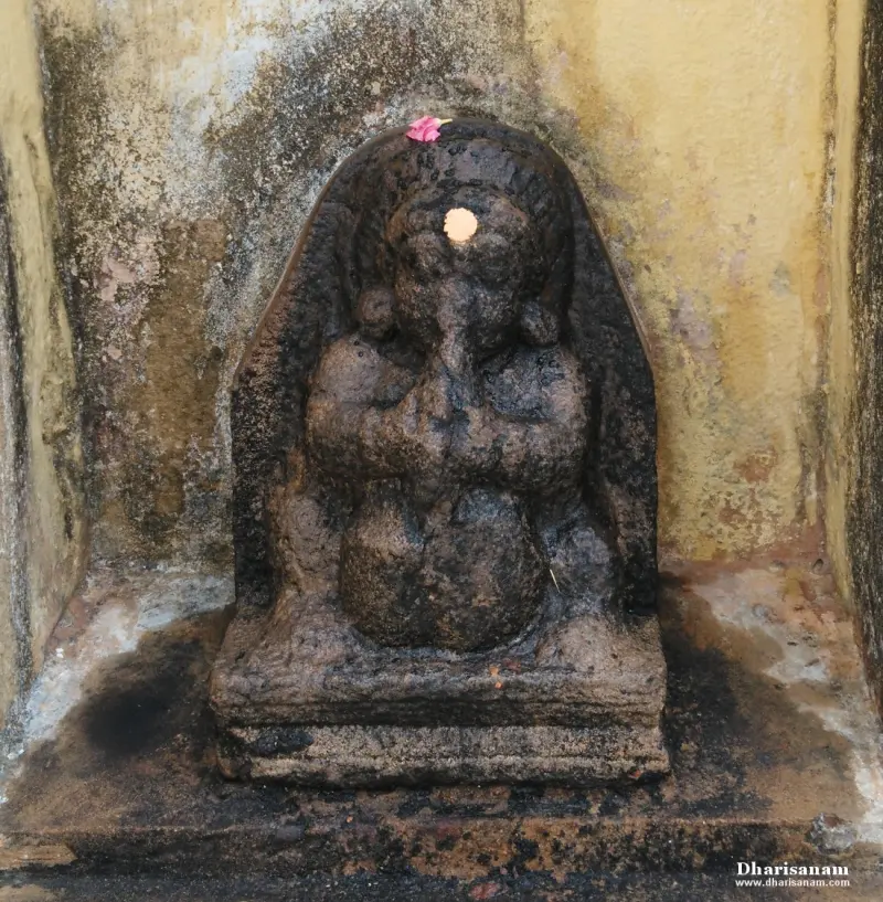 Dark stone Vinayakar with a flower on the head and a mark on the forehead, seated on a stepped base