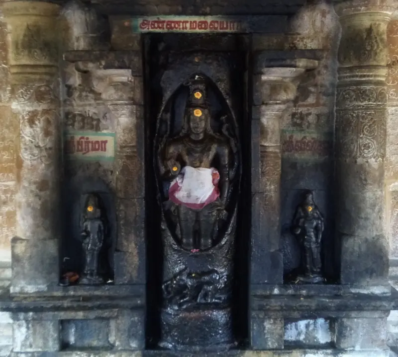Dark stone figure with a white cloth in a carved niche, with a small figure on each side