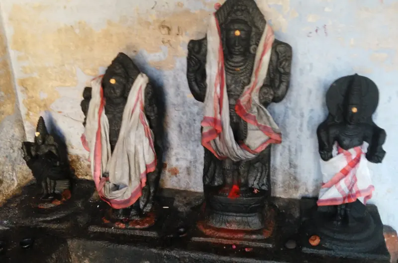 Four black stone idols draped in white and red cloth stand in a row before a stained wall