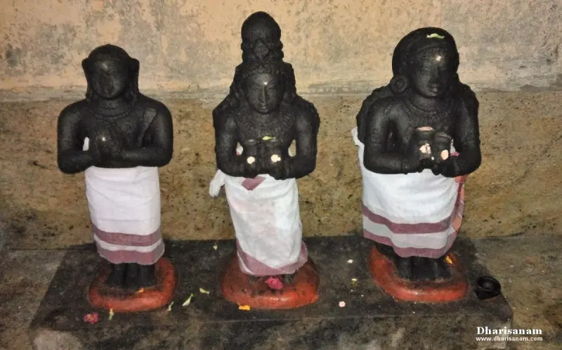 Three black stone figures in white dhotis with palms joined, standing on red bases