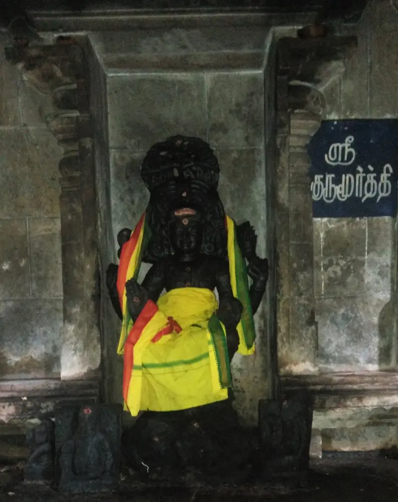 A dark standing figure in a niche, draped in yellow and green cloth