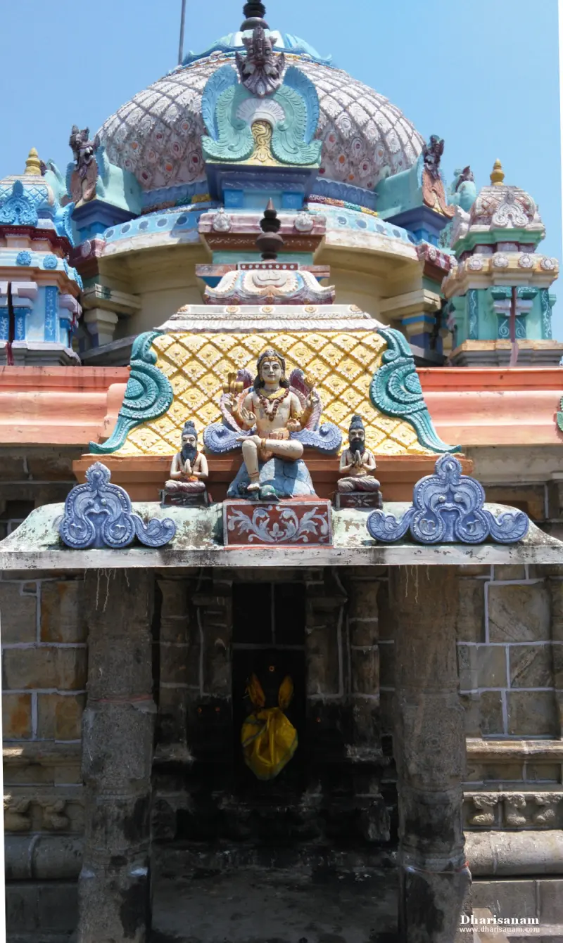 A stone shrine front under a colourful roof, with a seated figure between two bearded sages and a yellow cloth inside