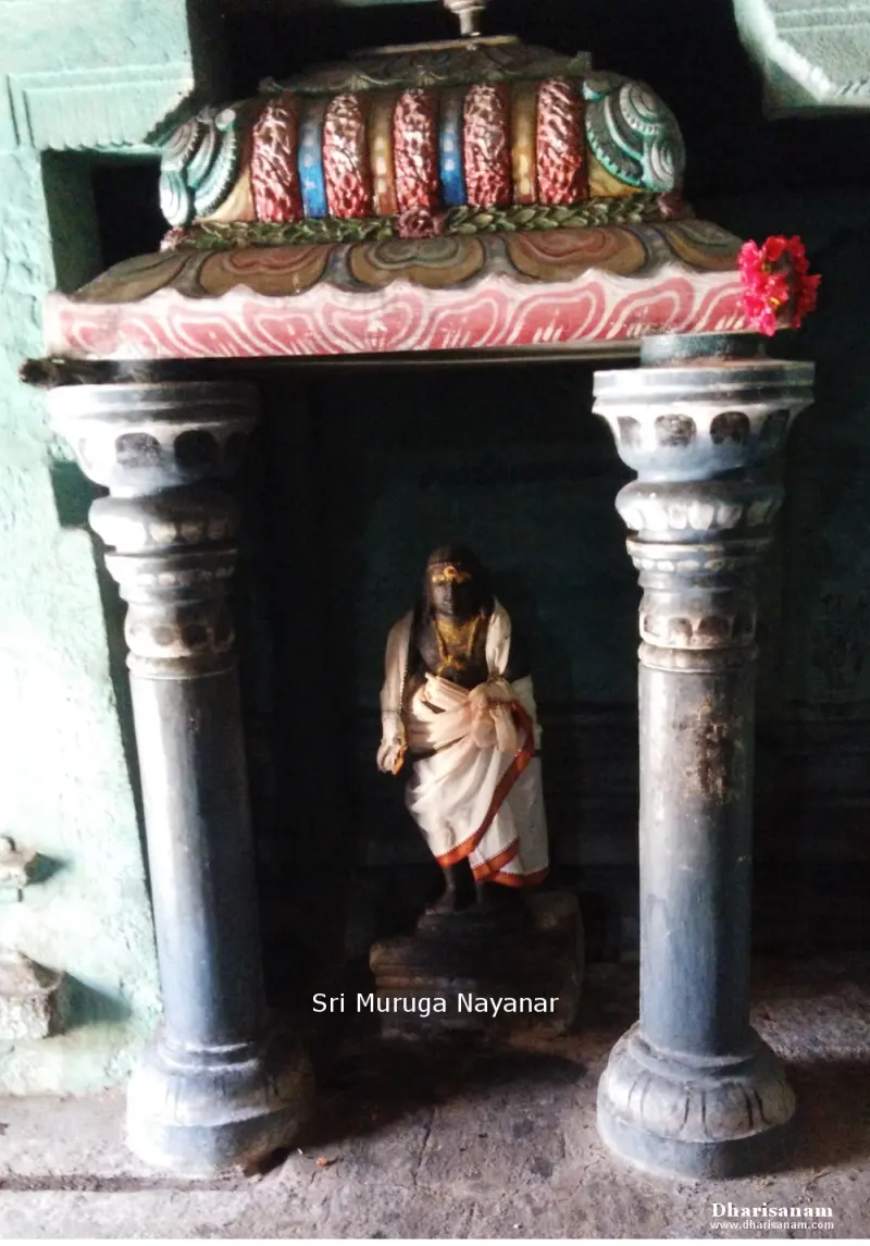 A small standing figure in white cloth with a flower garland, framed by two pillars