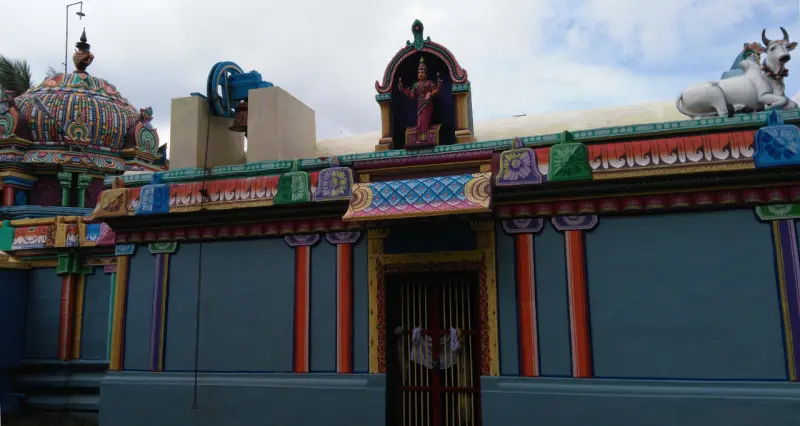 A blue shrine wall with a goddess figure in a niche above the door and a white bull on the roof