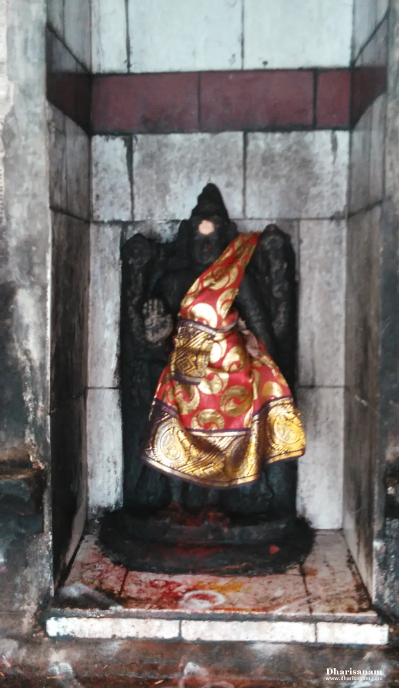 A seated dark idol with a raised hand, wearing a red and gold cloth.