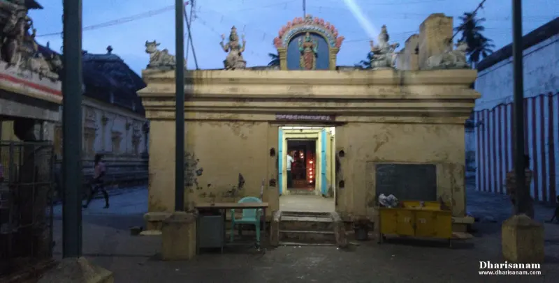 A yellow shrine with a lit doorway and a sculpted goddess figure in an arch above it, seen at dusk.