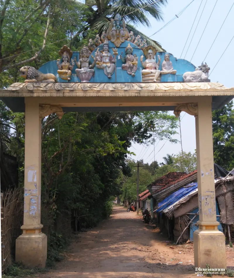 A pillared arch with painted figures on top, over a dirt road lined with trees and houses