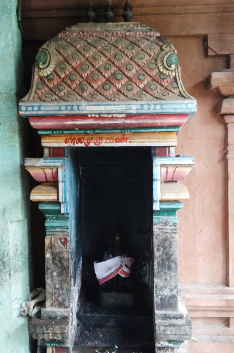 A narrow shrine with a painted tiled canopy and a Tamil name board, its idol wrapped in cloth