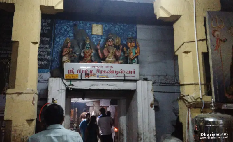 A doorway with a name board and painted figures above it, with devotees walking in.
