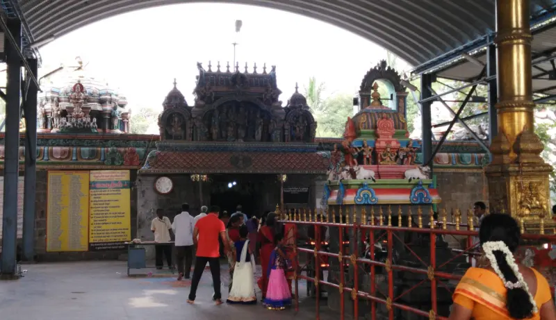 Devotees in a covered hall, with a gold flagstaff, a railing and painted shrine towers beyond.
