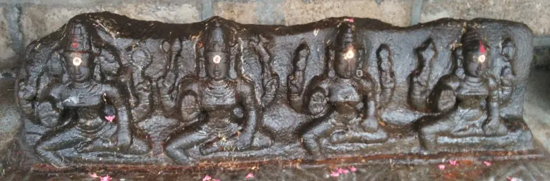 A dark granite slab carved with four seated figures, each with a dot on the forehead