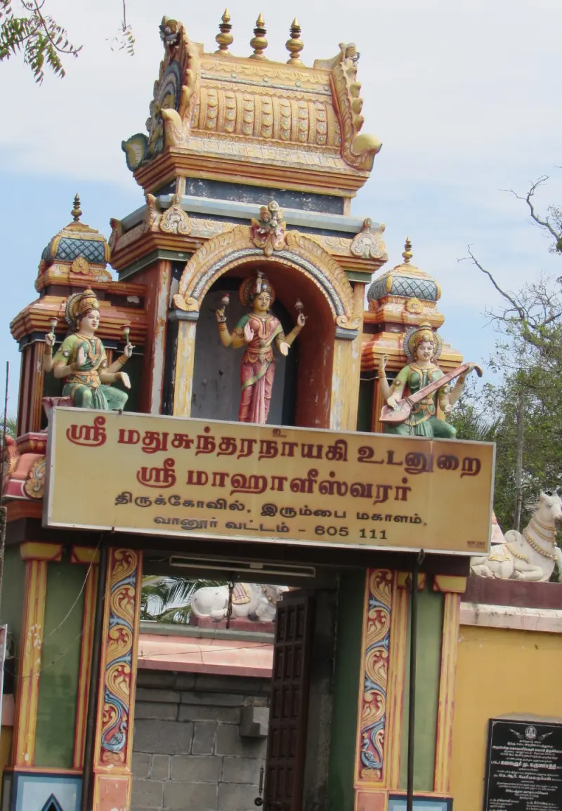 A colourful entrance gateway with painted figures above a Tamil name board, and a wooden door below.