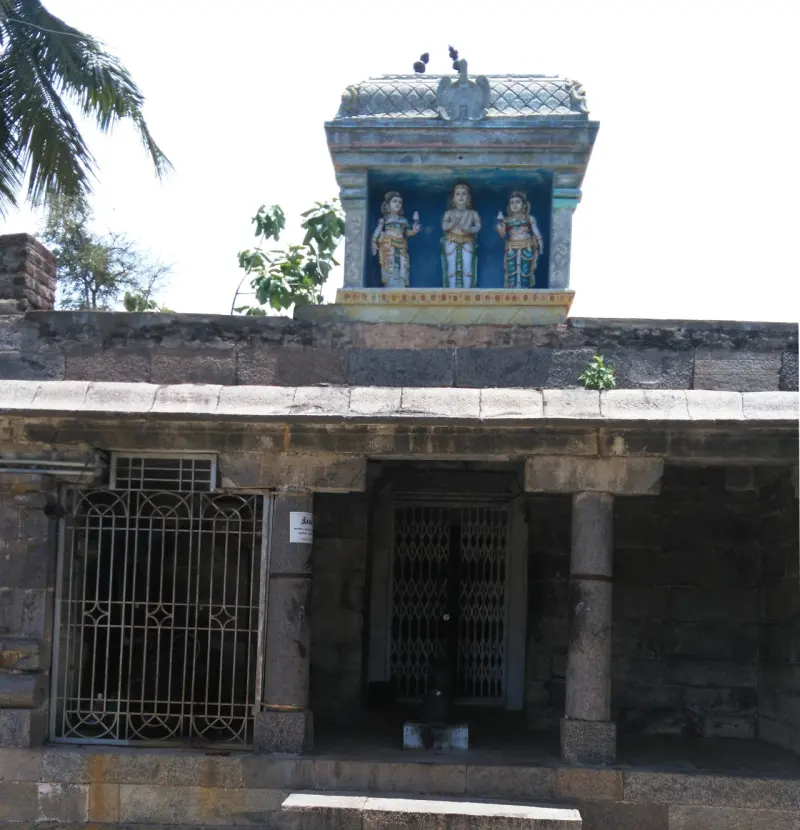 A stone shrine with iron grilles; on its roof, a blue niche holds three painted figures.