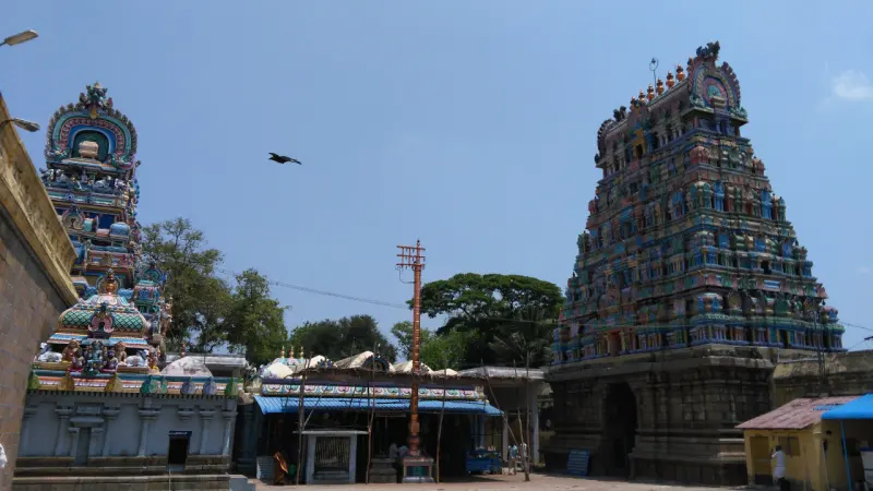 A courtyard view with a tall flagstaff under a blue canopy, and a painted gopuram rising on the right