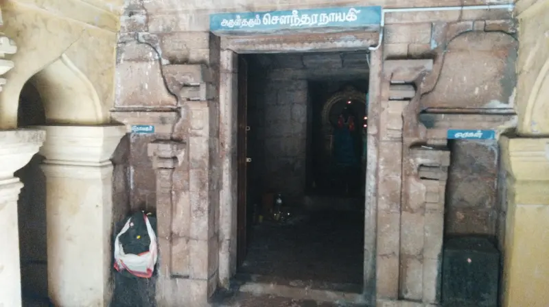 Stone doorway under a blue Tamil name board, with a dim shrine inside