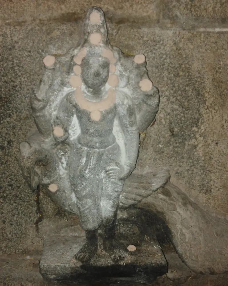 A small grey stone Murugan with a peacock behind, marked with pink powder