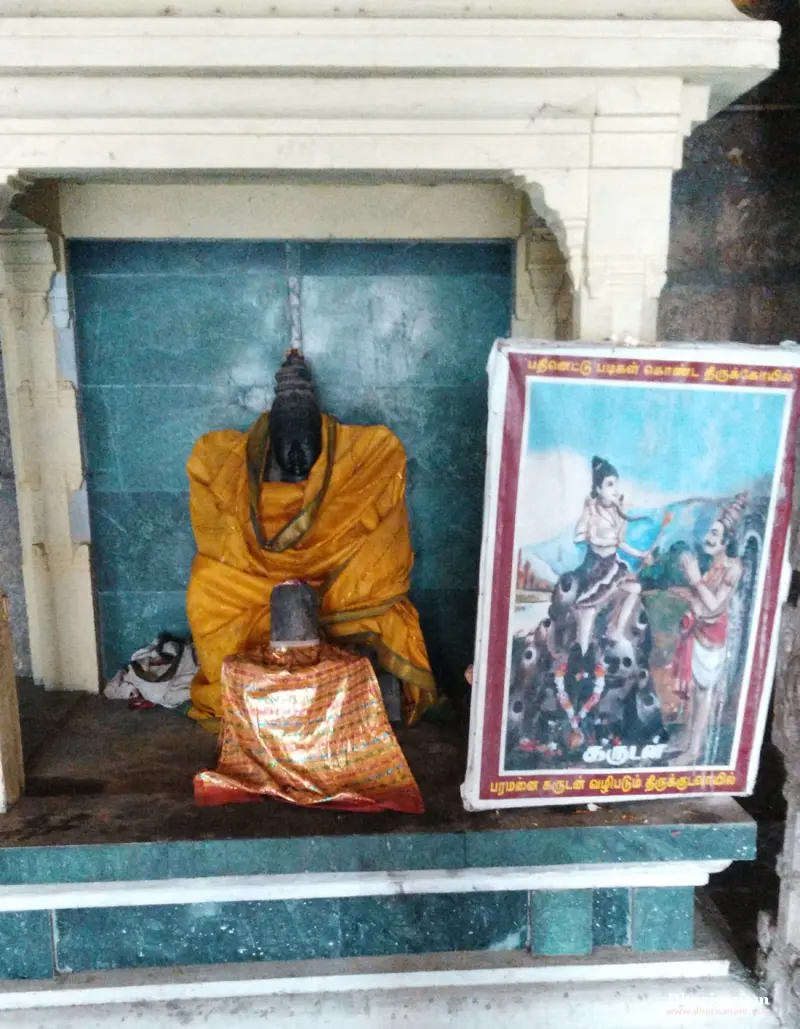 A draped idol in a shrine beside a framed Garudan picture