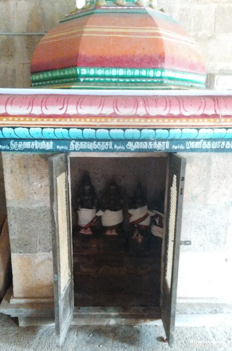A small shrine with a painted dome, open doors and four dark stone idols in white cloths inside