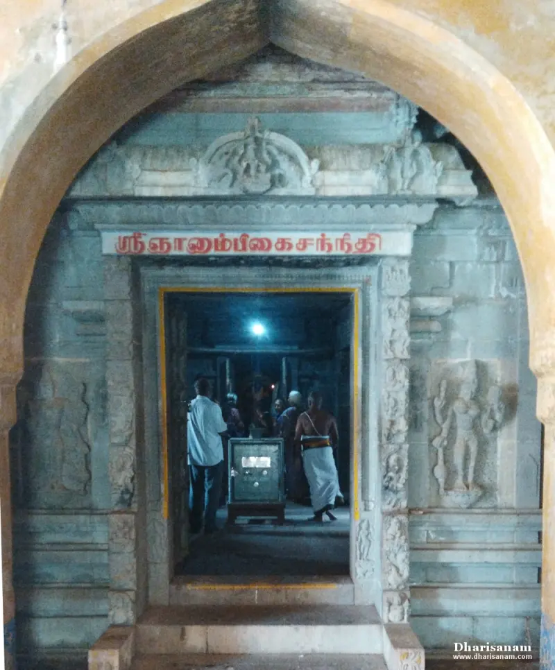 A stone doorway with a red Tamil name board, seen through an arch, with devotees inside