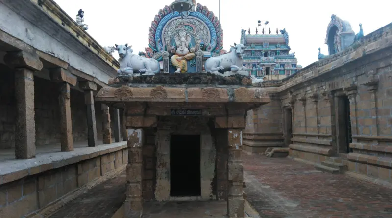 Small shrine with a painted Vinayakar and two bulls; tower and corridors in the background