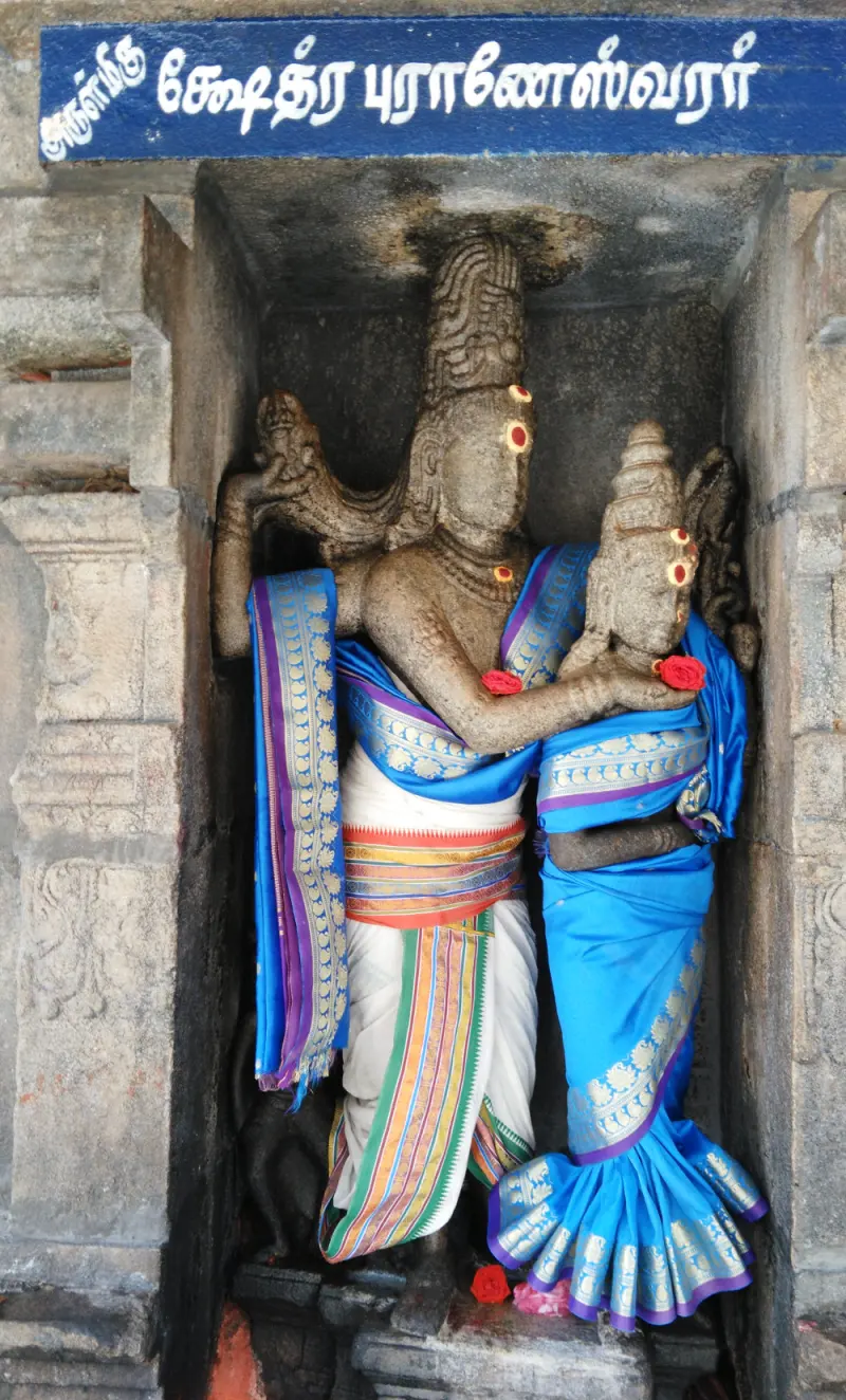 Stone Shiva holding Goddess Parvathi's cheek, dressed in silks, in a niche under a blue Tamil name board