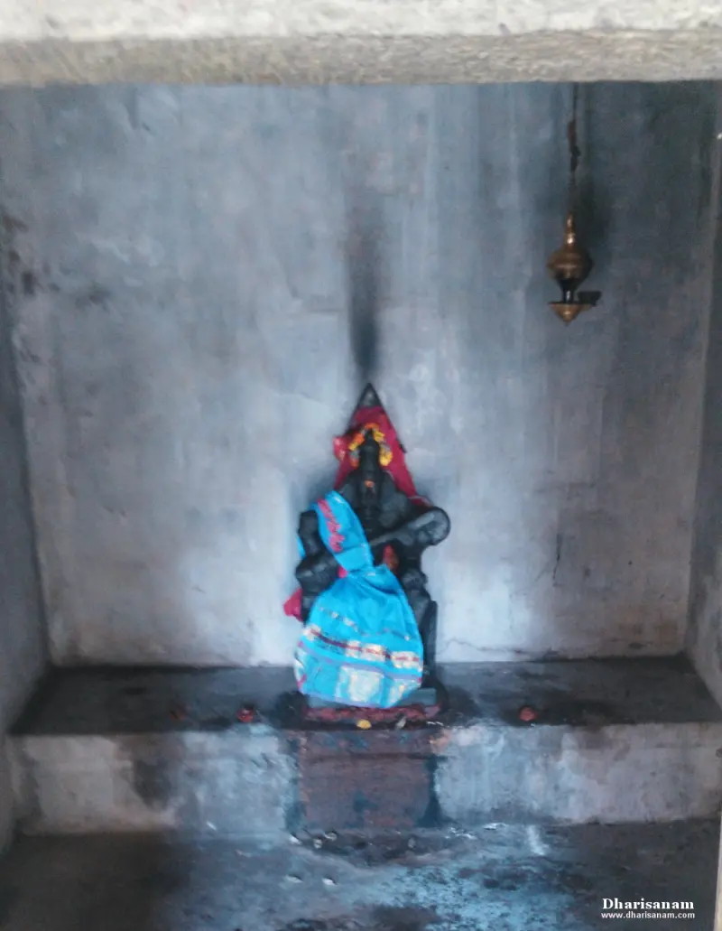 A small dark idol draped in blue and red cloth, in a bare stone recess with a hanging lamp