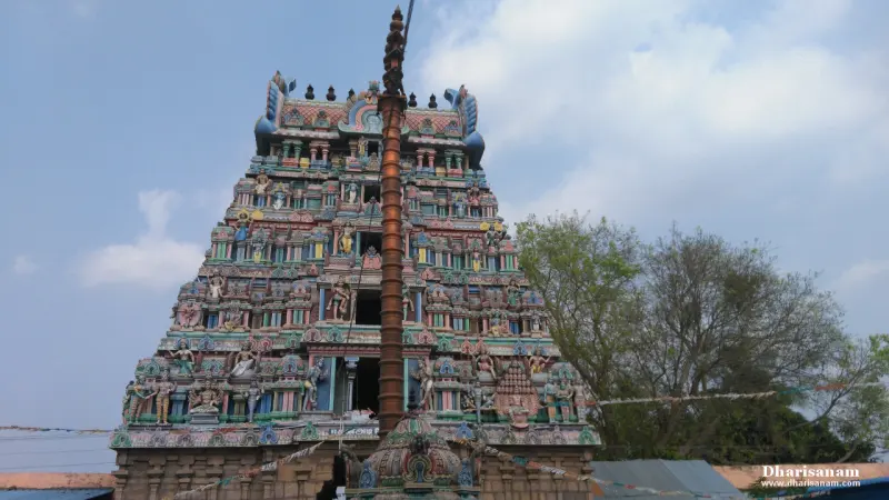 A multi-tiered tower with painted figures seen from below, a tall flagstaff in front of it, under a blue sky