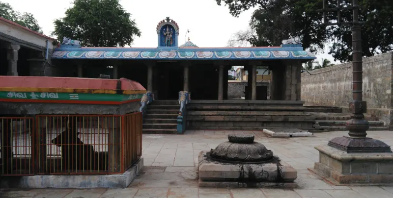 Paved courtyard with a stone lotus pedestal, a tall pillar on the right, and a caged shrine on the left