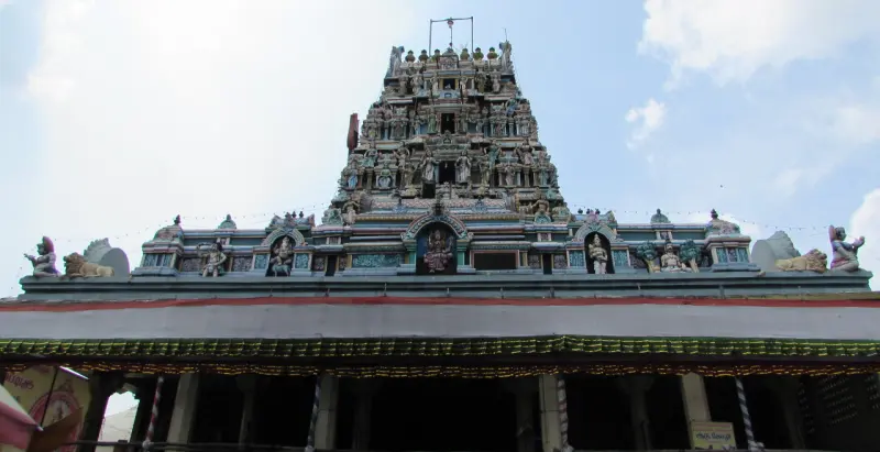A tiered gopuram rising above a pillared hall roof, with painted figures along the roofline.