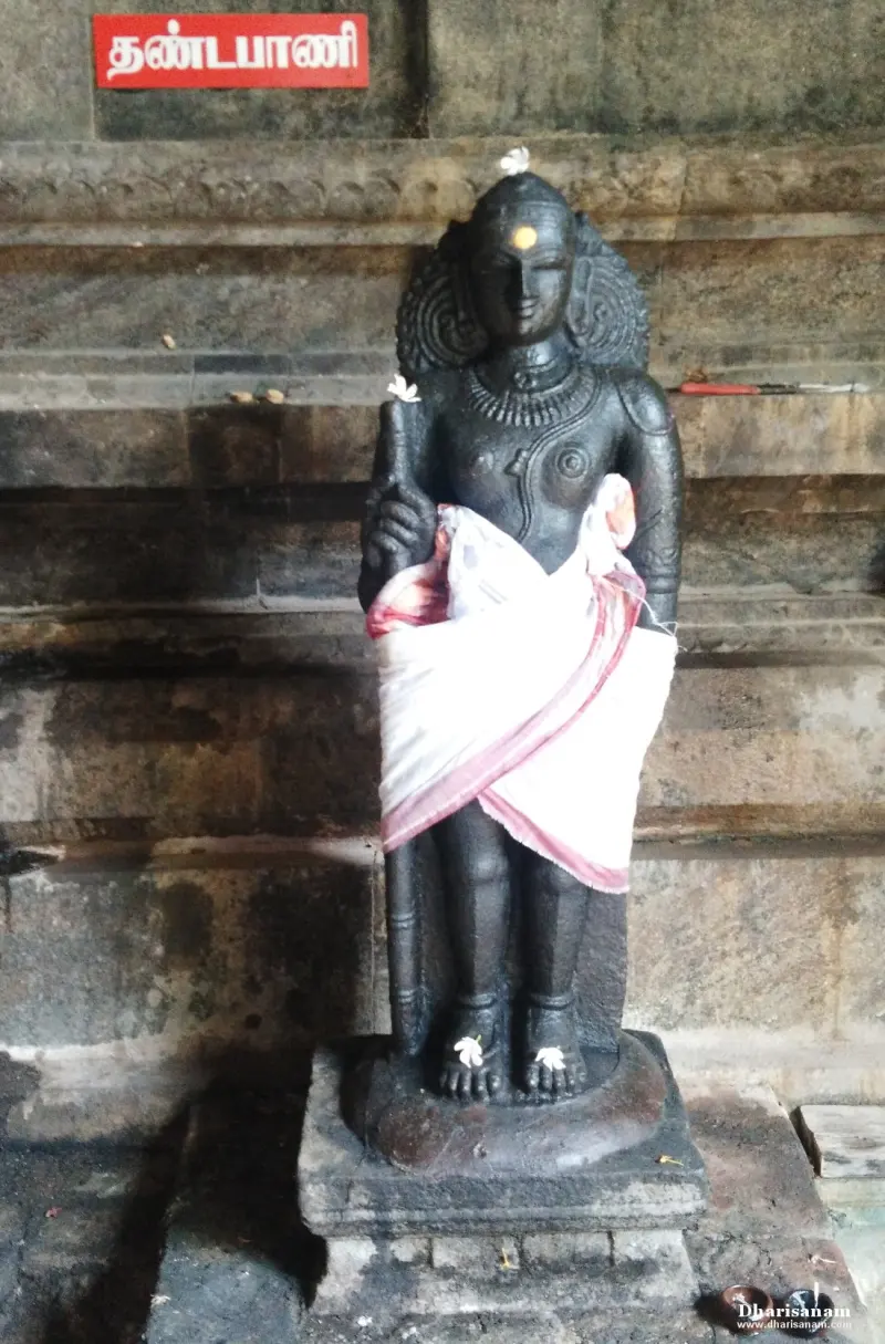 Standing dark stone idol with a staff, a white cloth at the waist and a Tamil name board above