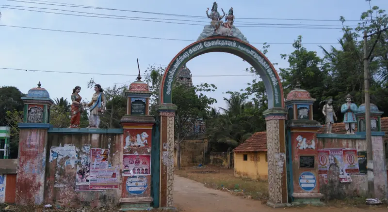 A painted arch with figures on its pillars and top spans a village road, with trees and houses beyond