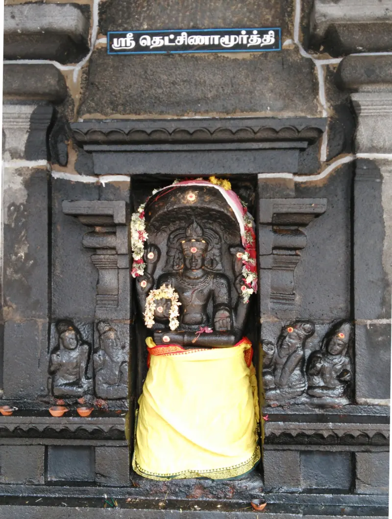Black stone Dakshinamurthy in a niche, dressed in a yellow cloth and garlanded