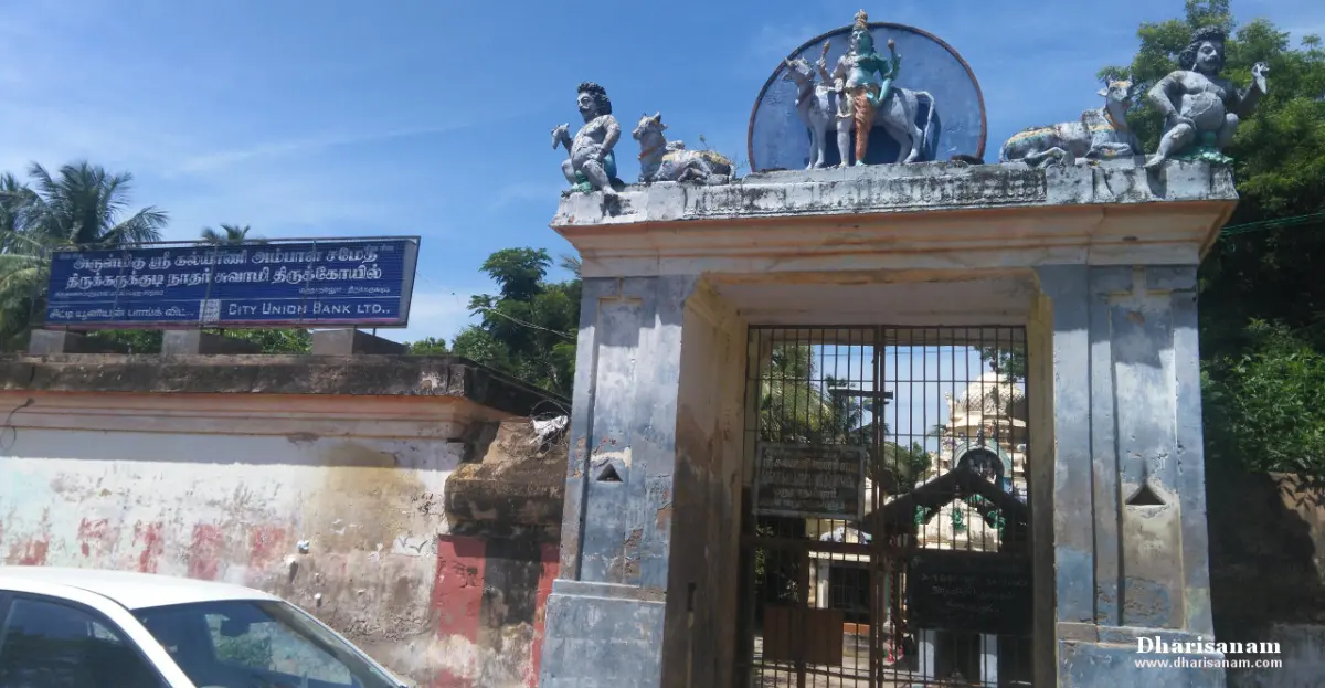 A temple gate topped by Shiva on Nandhi, with guardian statues and a signboard beside it