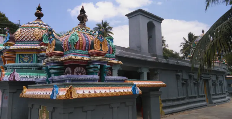 Painted shrine domes in the foreground and a long grey corridor wall with a small tower, under a blue sky