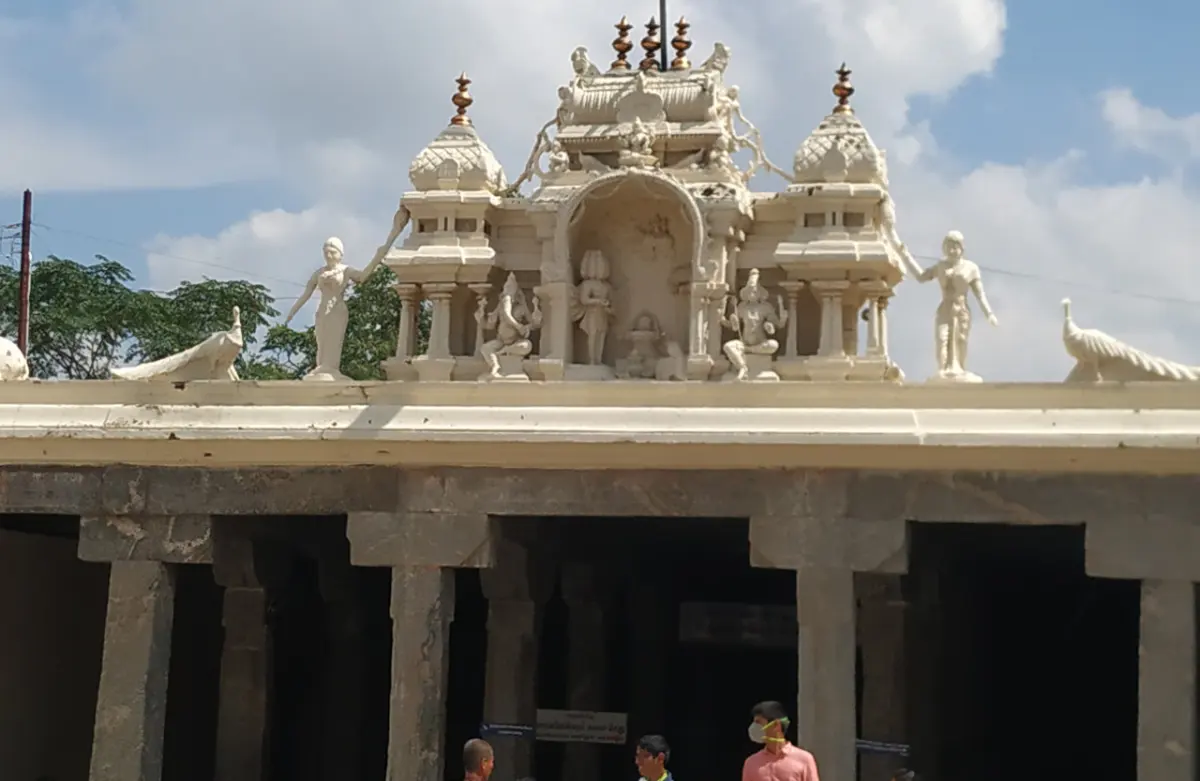 A pillared stone hall with a small white tower and statues on its roof, with a few people at the bottom.