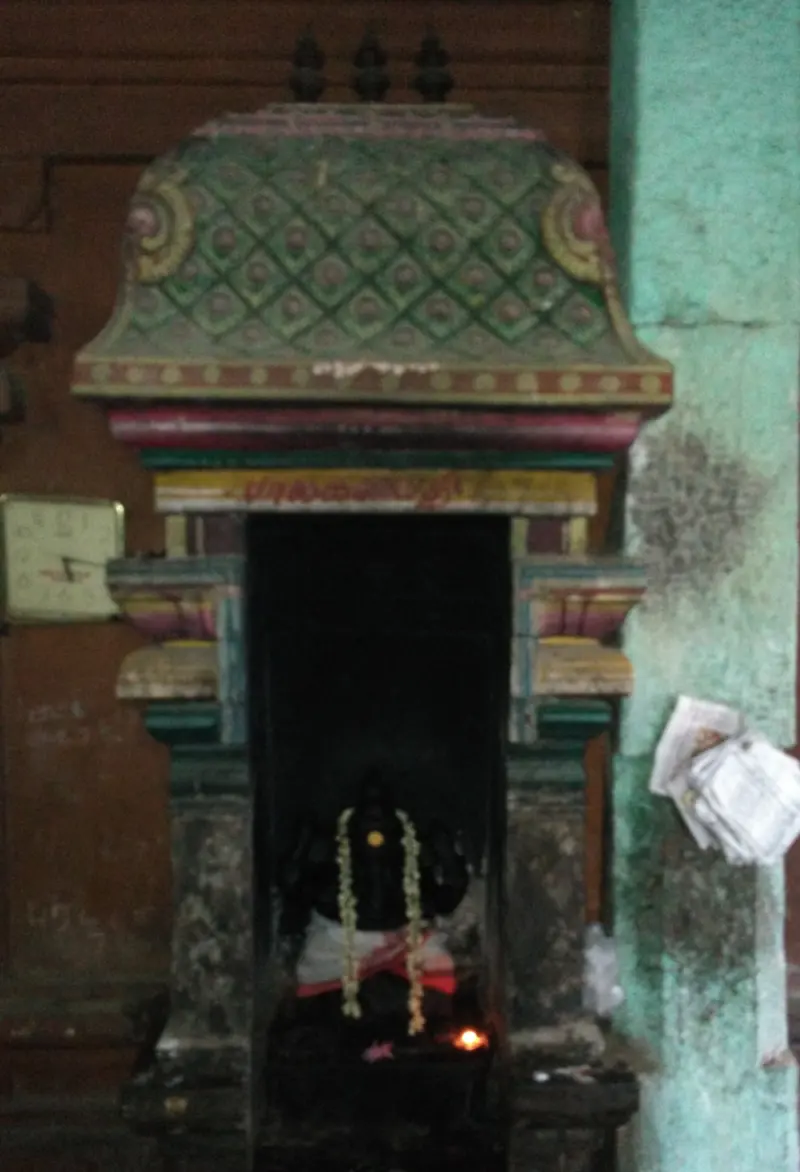 A painted shrine niche with a lamp burning before a dark idol hung with jasmine garlands