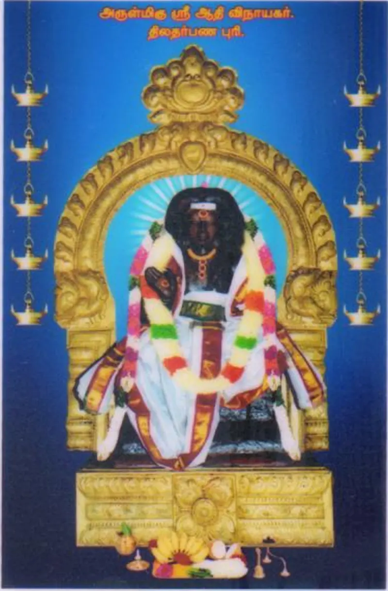 A garlanded dark idol seated on a golden arched throne, with hanging lamps on both sides and a blue background.