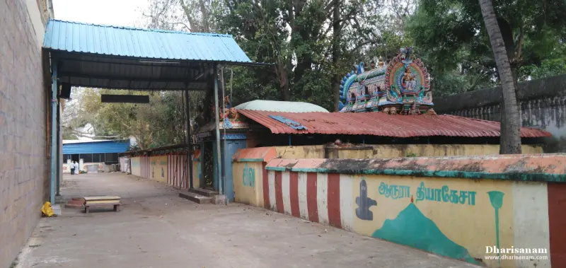 A paved passage with a roofed shelter on the left and a low painted wall on the right, a small shrine roof beyond