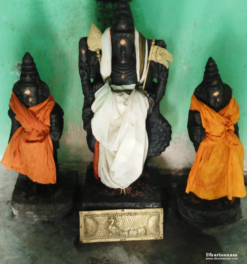 A central figure holding a spear and a flag, flanked by two smaller idols in orange cloth, a brass peacock plate below