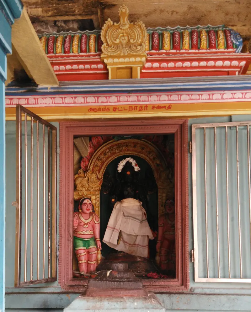 A shrine niche with a cloth-draped figure and two painted attendants; the sign reads Sattanathar Sannadhi